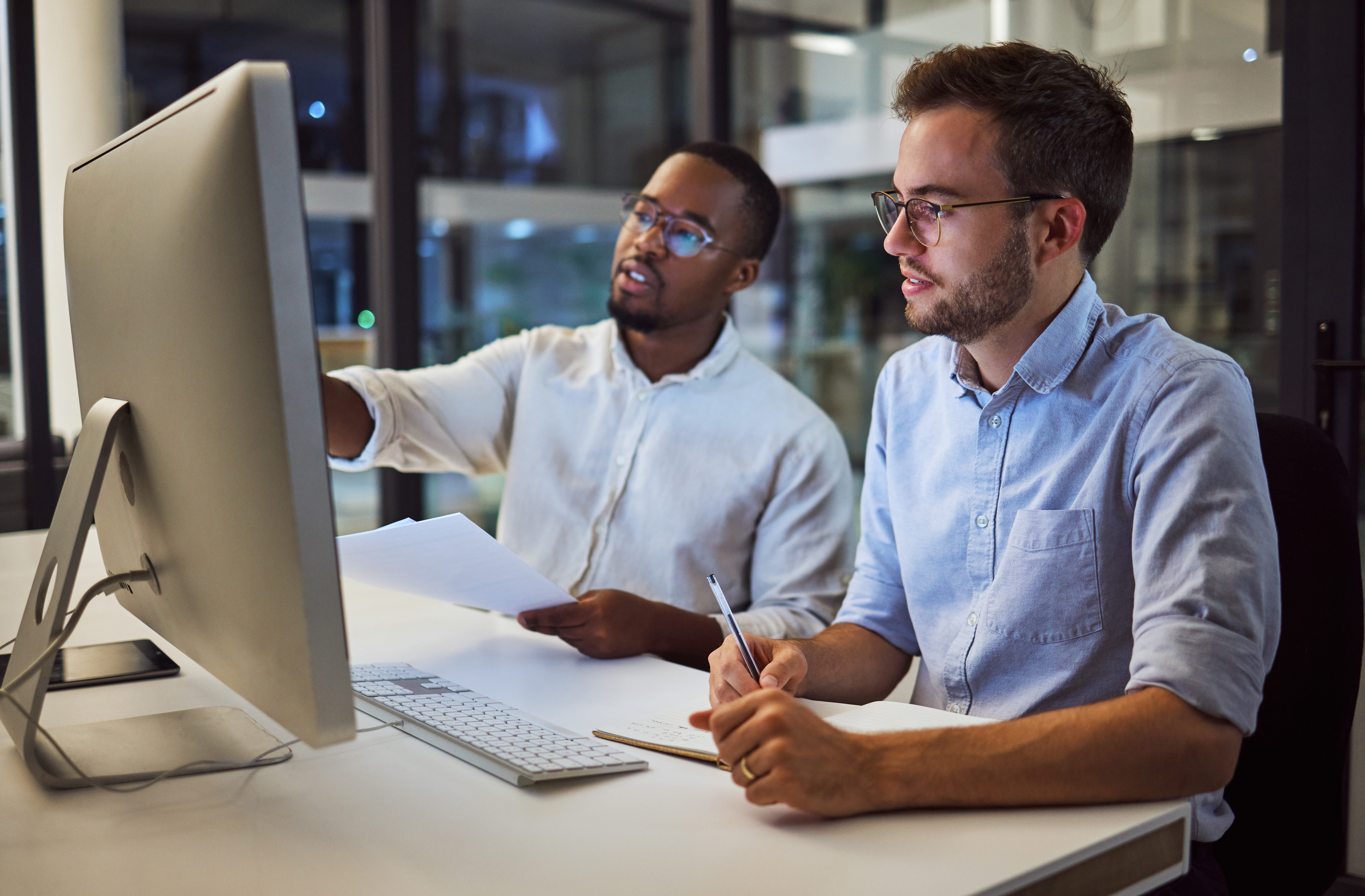 Two gentlemen seated at a desk looking at a computer. 